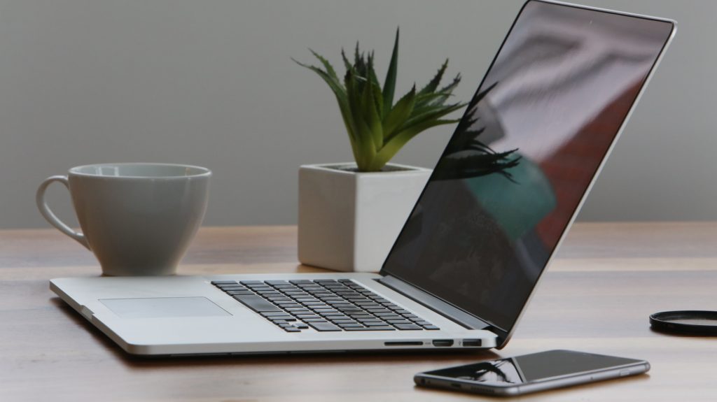 Silver laptop sitting alongside a coffee cup, smartphone and desk plant