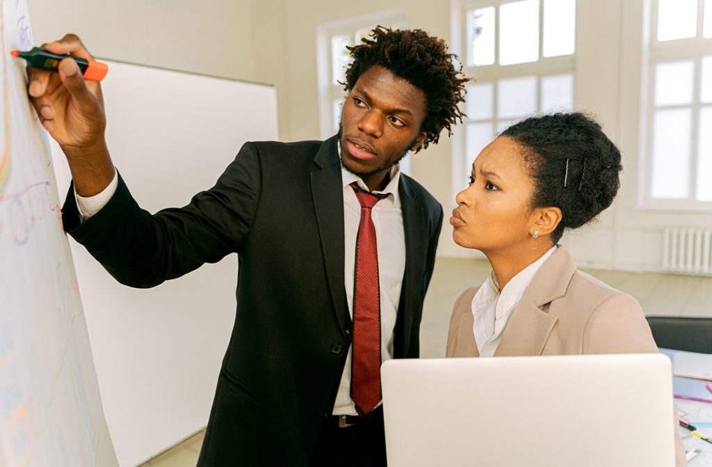 Class mates working together on white board to solve a problem
