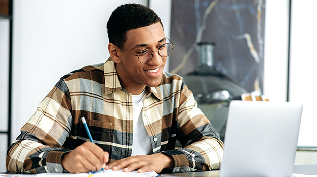 Man doing an online course on laptop, taking notes.