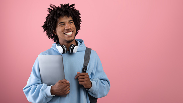 Systems developer student holding laptop in hand whilst smiling with backpack